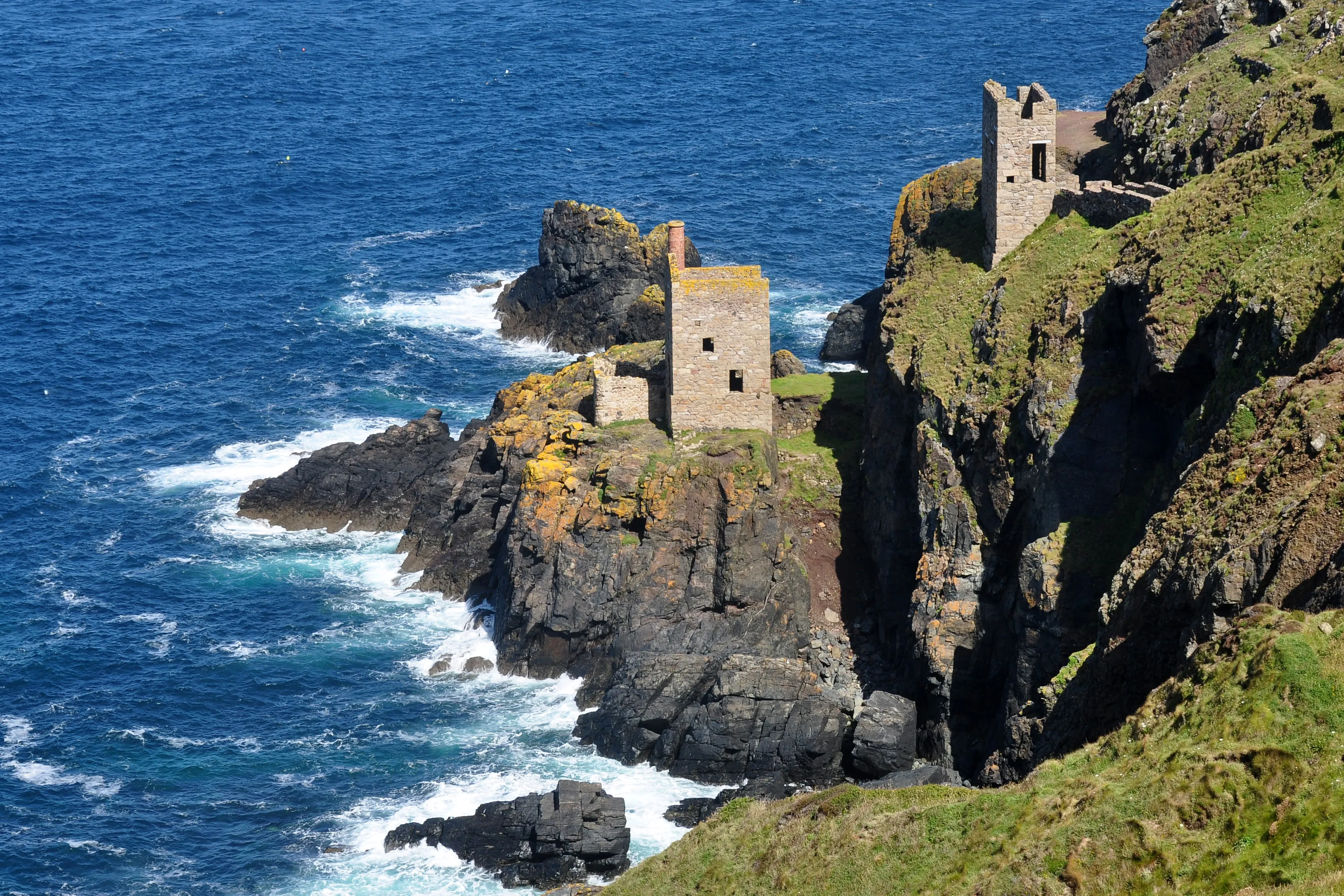 Two ruined stone engine houses on the cliffs at Botallack, with the Atlantic breaking on the rocks below