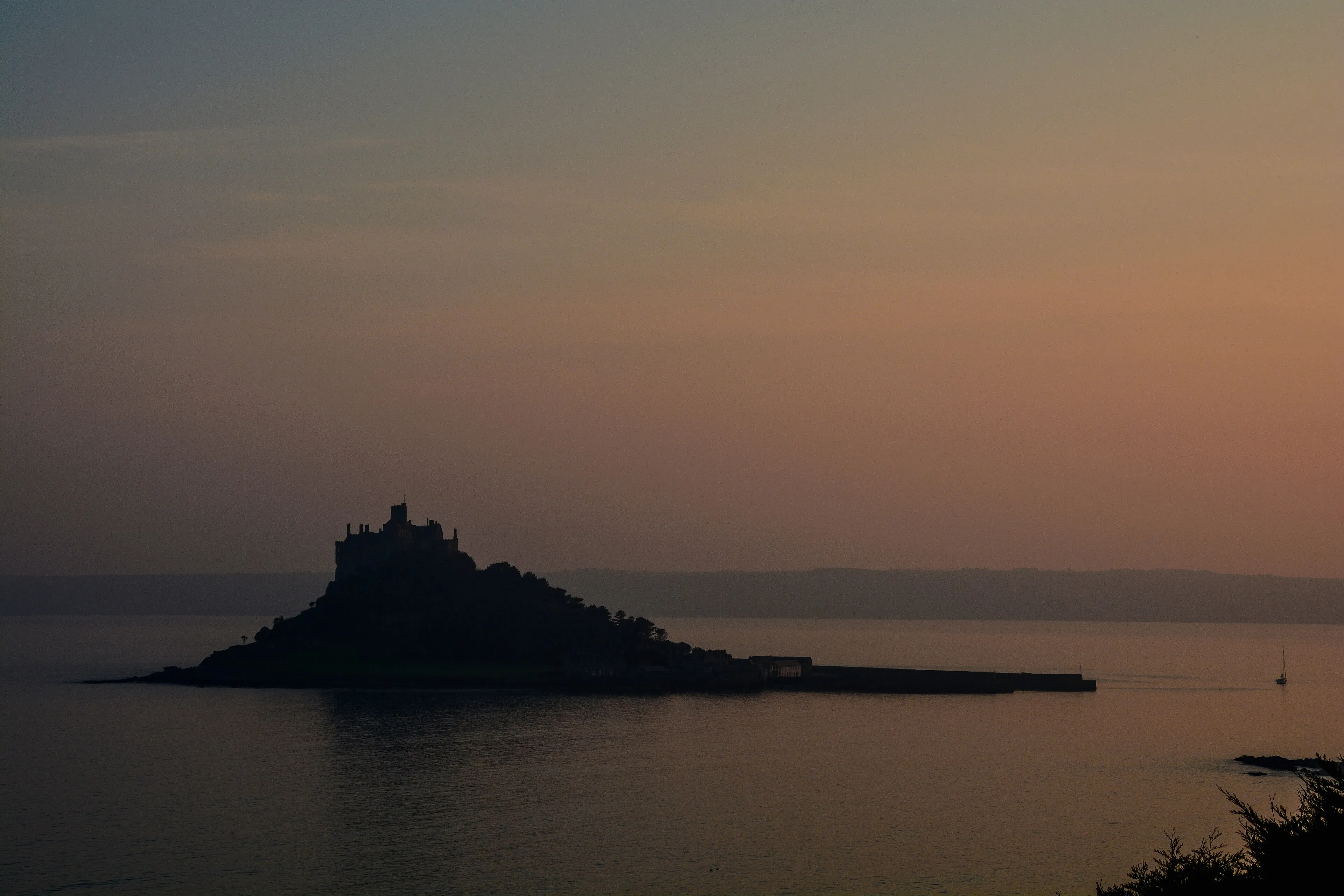 St Michael's Mount in silhouette across a calm bay at dusk